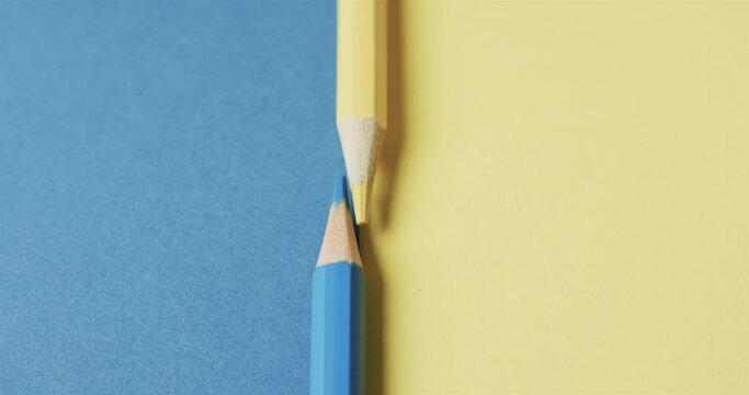 Close up of yellow and blue crayons with copy space on blue and yellow background, in slow motion