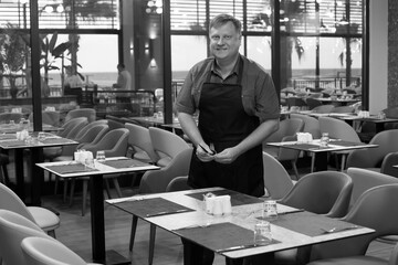 An adult waiter in a restaurant sets the table, black and white photo.