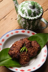 Tempe Bacem is tempeh cooked with coconut water, brown sugar, bay leaves, galangal, shallots, garlic, and coriander. Indonesian food. Served on a vintage plate.