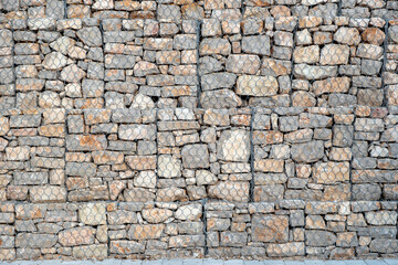 Empty grey stonewall behind wire metal mesh for protection background texture. Copy space