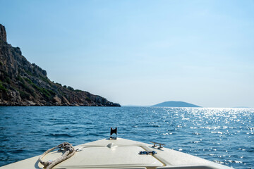 Moored yacht in sparkle ripple sea, Greece. Land ahead, clear blue sky, view from the boat bow.