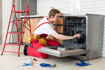 Technician or worker in uniform installs dishwasher into the kitchen furniture. Repairman wear...