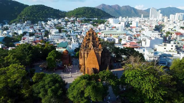 Aerial approach Po Nagar Cham temple red tower Vietnam Nha Trang sunny cityscape. Authentic culture Asia. Modern buildings city bridge active road traffic river fishing old boats. Religion buddhism