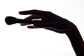Close-up silhouette of a makeup brush in a woman hand on a white background.