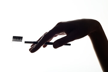 Close-up silhouette of a cosmetic eyebrow brush in a woman hand on a white background.