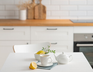 Fototapeta na wymiar A cup of tea with lemon and a teapot on a white table.