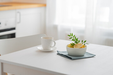 A cup of tea with lemon and a teapot on a white table against the background of a white kitchen...