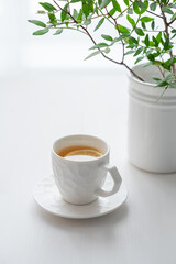 A cup of tea with lemon and green branch on a white table against the background of a kitchen window.