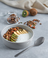 Healthy granola with yogurt, banana and kiwi in a bowl on a light background.