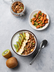 Flat lay of granola with yogurt, banana and kiwi in a bowl on a light background.