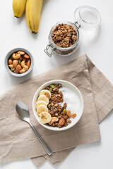 Granola or muesli with yogurt and banana on a white wooden table.
