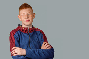 A red-haired teenager stands with a serious look, arms crossed over his chest and looks sternly at...