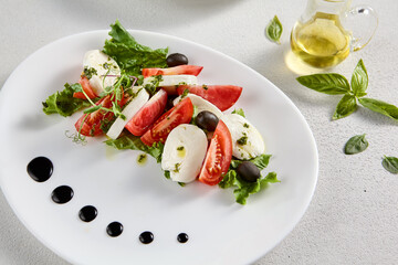 Classic Caprese salad with ripe tomatoes, mozzarella, and olives, garnished with fresh basil. Suitable for Italian cuisine promotions and cookbooks