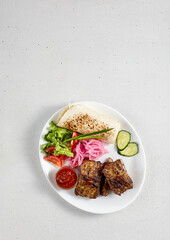 Grilled pork ribs with vegetable garnish and flatbread, served on a white plate, ideal for barbecue and culinary art concepts