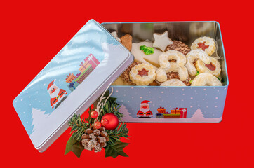 Weihnachtsbäckerei in einer bunten Keksdose mit  Weihnachtsdekoration vor einem roten Hintergrund