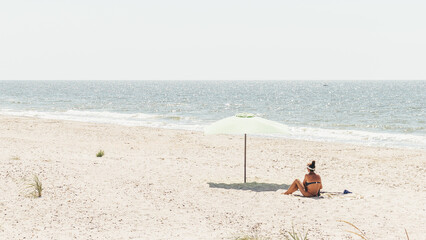 Fototapeta na wymiar Rear view of a young woman sitting with an umbrella on the beach during a summer vacation