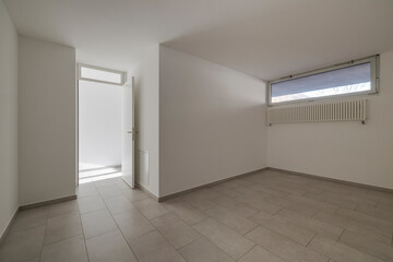 Room with white walls and a small window and an open door leading to the corridor