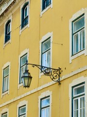Fototapeta na wymiar Vintage facade of yellow colour with decorated metallic street lamp on it in Lisbon, Portugal. Vertical photo