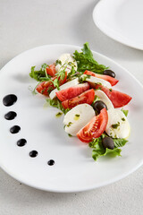 Classic Caprese salad with ripe tomatoes, mozzarella, and olives, garnished with fresh basil. Suitable for Italian cuisine promotions and cookbooks