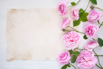 Pink roses, flowers and paper for congratulations on a wooden background. Postcard for the holiday.