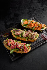 Gourmet bruschetta set with salmon, roast beef, and tuna on a black plate, side angle view