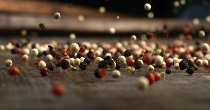 Super slow motion macro of dry mixed flavorful and aromatic peppercorn seeds falling on wooden table in rustic kitchen at 1000fps.