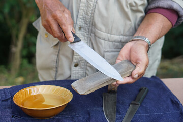 Closeup man hands sharpen knife on whetstone sharpener or grindstone. Concept, maintenance tools for cooking, make knife sharp ,not dull for long live using. Original style.  