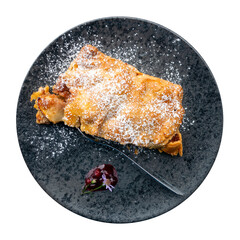 Delicious crispy apple strudel dessert isolated against white background. Served on black plate decorated with wild flowers and jam.