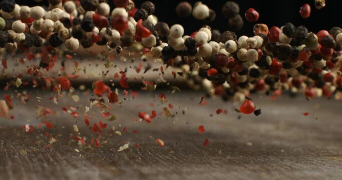 Super slow motion macro of dry mixed flavorful and aromatic peppercorn seeds is flying isolated on soft rustic wood background at 1000fps.