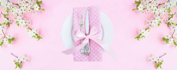 White plate, knife, fork and white flowering tree branches on the pink background. Top view. Copy...