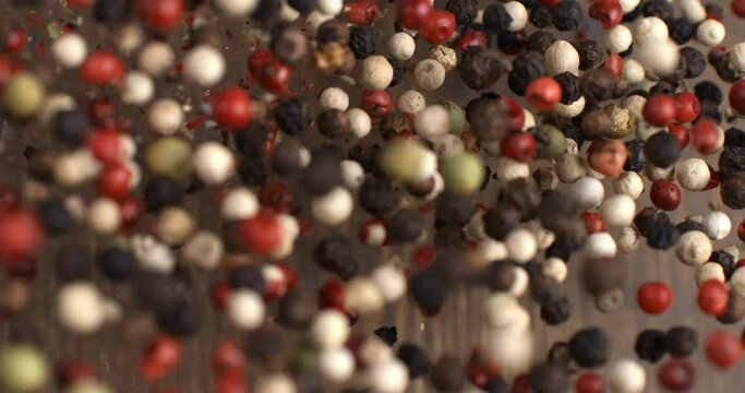 Super slow motion macro of dry mixed flavorful and aromatic peppercorn seeds is flying isolated on soft rustic wood background at 1000fps.