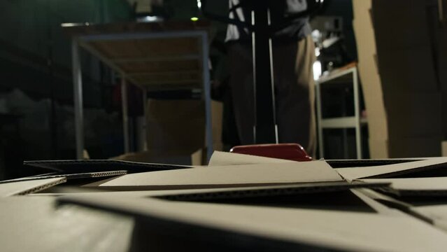 Loader maneuvers truck filled with cardboard boxes in warehouse. Worker in warehouse utilizes hand pallet stacker to transport packages