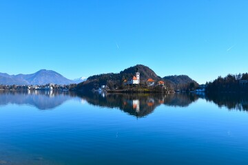 Church on the island of lake Bled in Slovenia and a forest covered hill behind in winter