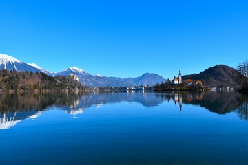 View of the church on the island at lake Bled and the castle on a hill above with a reflection in the water