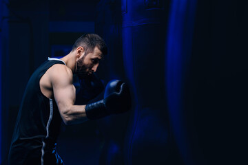 Male boxer trains punches on punching bag, dark background. Concept banner sport boxing