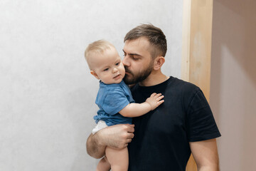 Father hugs baby boy, young man kisses his son on head in living room. Concept lifestyle parenting...