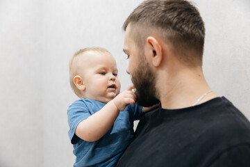Father hugs baby boy, young man kisses his son on head in living room. Concept lifestyle parenting fatherhood moment
