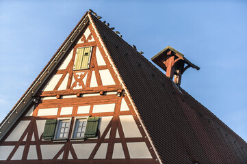Fototapeta na wymiar Giebelseite Fachwerkhaus mit Sprossenfenstern und Fensterladen und Glockenstuhl und Ziegeldach mit Tauben vor blauem Himmel