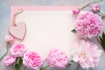 Pink roses, peonies flowers, heart and paper for congratulations on a wooden background. Postcard, letter for the holiday.