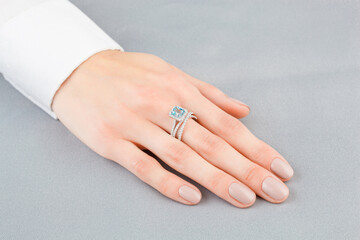 Beautiful female hand with gold ring with diamonds and aquamarine on gray background