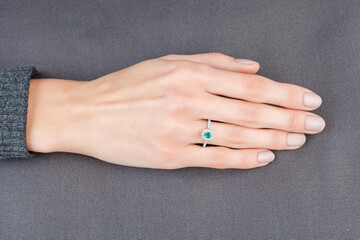 Beautiful female hand with gold ring with diamonds and emerald on gray background