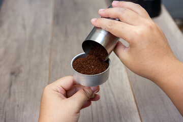 Aromatic roasted coffee beans fill a coffee powder container held in a hand, creating a close-up...