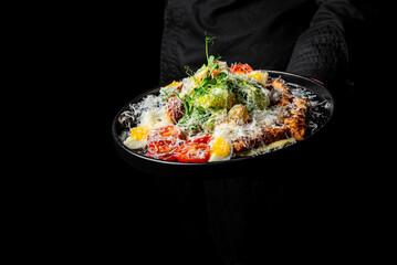 Men's waiter hands hold a Caesar salad with croutons, cheese, eggs, tomatoes and grilled chicken in pub