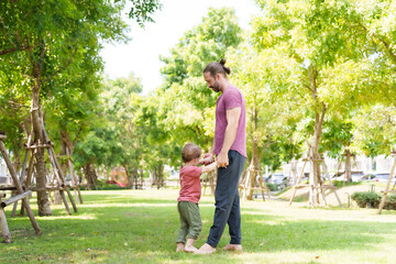 Caucasian father mother hold their little son hand, holding each child's hand lifting up, father mother take their adorable son for walk in picnic park on nice, sunny day, three feet touched grass.