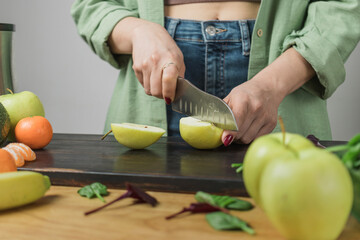 Woman cutting apple, preparing healthy vegan smoothie with spinach leaves, banana and avocado on a...
