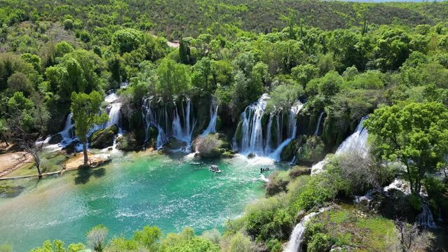 Aerial view of Kravica Waterfall in Bosnia and Herzegovina. People enjoying themselves on the boats next to the waterfall. Unique natural beauty in the Trebizat River for holidays and leisure time.