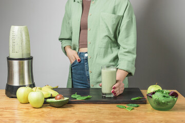 Unrecognizable woman in casual wear holding glass of fresh blended healthy green vegan smoothie....