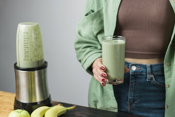 Unrecognizable woman in casual wear holding glass of fresh blended healthy green vegan smoothie....