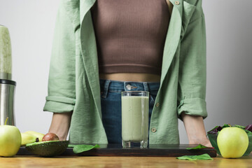 Unrecognizable woman in casual wear with glass of fresh blended healthy green vegan smoothie....