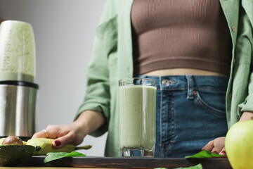 Unrecognizable woman in casual wear with glass of fresh blended healthy green vegan smoothie....